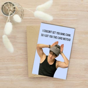 May include: A greeting card featuring a photograph of a man with his hands on his head making bunny ears. The text on the card reads "I couldn't get you Bang Chan, so I got you this card instead."