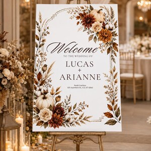 May include: A rectangular wedding welcome sign on a gold easel featuring the text Welcome to the wedding of Lucas + Arianne Sarah Gardens 123 Anywhere St., CA, ST 12345, decorated with an arch of watercolor pumpkins, cotton, and autumn flowers.