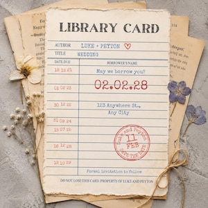 May include: A vintage-style library card wedding invitation printed on cream paper with deckled edges. The text includes "LIBRARY CARD," "LUKE + PEYTON," and "02.02.28." It features blue lines, red date stamps, a red circular "SAVE THE DATE" stamp, and dried flowers.