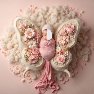 May include: A newborn baby is sleeping in a white butterfly-shaped prop decorated with pink flowers. The baby is wrapped in a pink blanket and is wearing a white hat.
