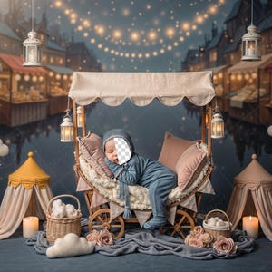 May include: A baby in a blue outfit sleeps in a wooden carriage with a canopy. The scene is set in a whimsical market with hanging lanterns, clouds, and stars. Decorative elements include pillows, baskets, and a small tent.
