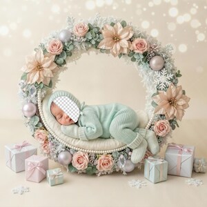 May include: A newborn baby in a light blue outfit rests inside a floral wreath with pink and white flowers, pearls, and ornaments. Several wrapped gift boxes and snowflakes are at the base of the wreath. The background is a soft, blurred beige.