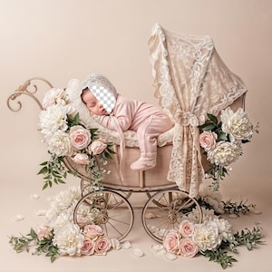 Könnte beinhalten: Ein Vintage-Kinderwagen mit einem schlafenden Säugling, geschmückt mit weißen und rosa Blumen. Der Kinderwagen hat ein Spitzendach und ist vor einem weichen, neutralen Hintergrund platziert. Der Wagen hat ein klassisches Design mit Speichenrädern.