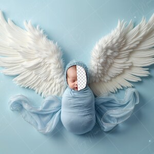 May include: A baby wrapped in a light blue blanket with white angel wings, wearing a white hat. The baby's face is obscured by a white cutout.