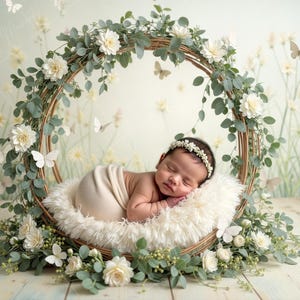 May include: A newborn baby girl sleeping peacefully in a white faux fur nest surrounded by a wreath of green leaves and white flowers. The nest is placed on a light wood floor.