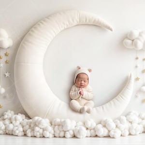 May include: A sleeping newborn in a cream bear hat and onesie, positioned on a large, cream crescent moon prop. The scene is decorated with white clouds, gold stars, and a white backdrop, creating a dreamy, celestial theme.