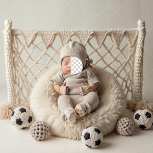 May include: A newborn baby wearing a beige knitted hat and outfit is sleeping in a white faux fur nest. The nest is in front of a macrame wall hanging that resembles a soccer goal. There are several crocheted soccer balls around the nest.