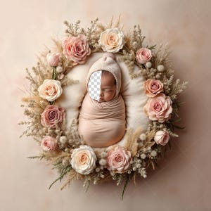 Może przedstawiać: Noworodek owinięty w miękki, brzoskwiniowy kocyk i czapeczkę, osadzony w wieńcu kwiatowym z róż i suszonych traw. Wieniec ułożony jest na kremowej poduszce, tworząc spokojną i naturalną estetykę.