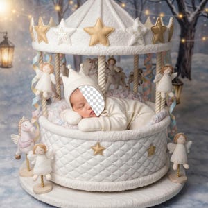 May include: A newborn baby in a white outfit and crown sleeps peacefully inside a carousel-themed crib. The crib is white with gold star accents and angel figurines. The background is a winter scene with lanterns.