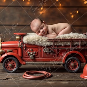 May include: A newborn baby sleeping on a red toy fire engine with a white fur blanket. The engine has a ladder and a hose. There are two red fire helmets on the floor.