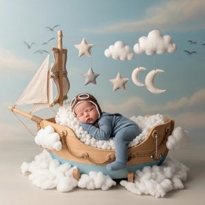 Può includere: Un bambino che dorme, vestito con un completo blu e un cappello da aviatore, riposa in una barca a vela di legno. La barca è su un letto di soffici nuvole bianche, con stelle, lune e nuvole appese sopra. Lo sfondo è un cielo con nuvole e uccelli.