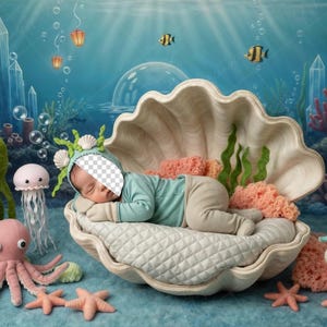 May include: A newborn baby in a sea-themed photo setup. The baby is dressed in a blue outfit and resting in a large seashell. The scene includes coral, starfish, an octopus, and a jellyfish. The background is an underwater scene with fish and bubbles.