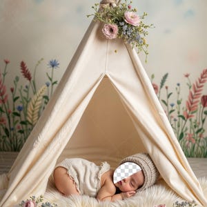 Op de afbeelding: Een crèmekleurige tipi-tent versierd met bloemen, met een baby die een gebreide muts en romper draagt, liggend op een zacht wit tapijt. De tent is versierd met roze en blauwe bloemen.