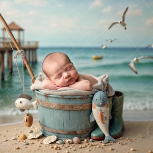 Könnte beinhalten: Ein Baby schläft in einem blauen Holz-Eimer mit einem Spielzeugfisch, der an einer Angelrute hängt. Der Eimer steht auf einem Sandstrand mit Muscheln und einem blauen und weißen Spielzeugfisch.