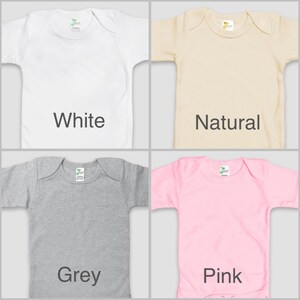 four different colored baby shirts, each with a label indicating the color: white, natural, grey, and pink.