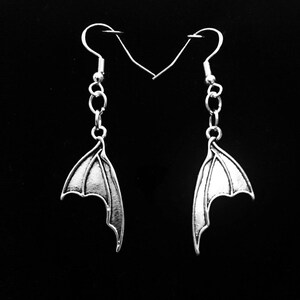 May include: A pair of silver earrings featuring a wing design. The wings are detailed and have a slightly textured finish.