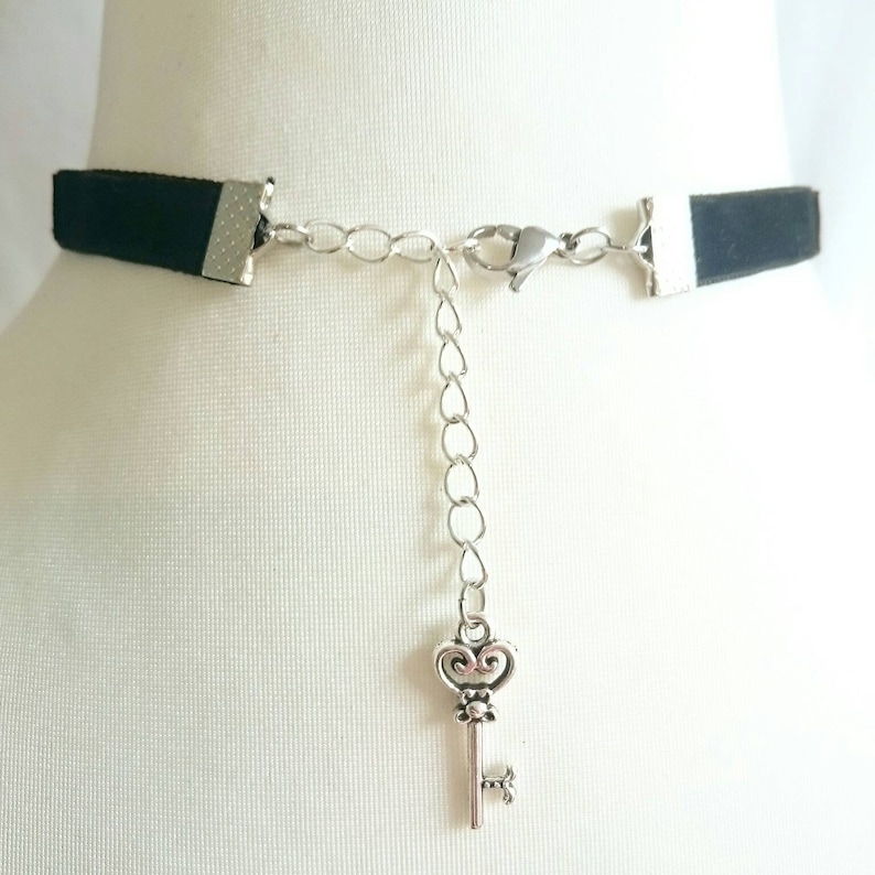 May include: A black velvet choker necklace with a silver chain and a key charm. The chain is adjustable and the key charm is a decorative detail.