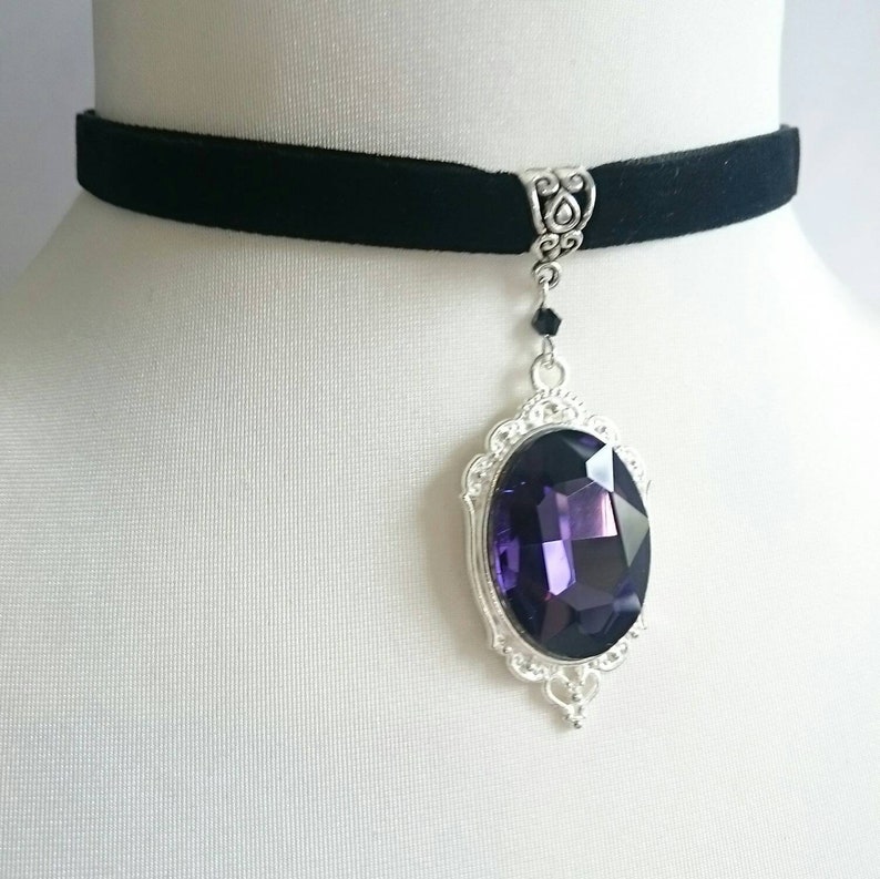 May include: A black velvet choker necklace with a silver pendant featuring a large, oval-shaped purple gemstone.
