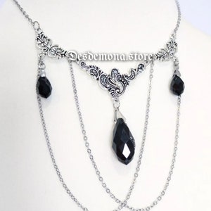 May include: Silver necklace with a decorative floral design and three black, teardrop-shaped pendants. The necklace has multiple strands of delicate chain and the text "Desdemona.store".