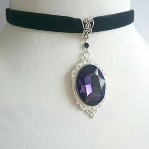 May include: A black velvet choker necklace with a silver pendant featuring a large, faceted purple gemstone.