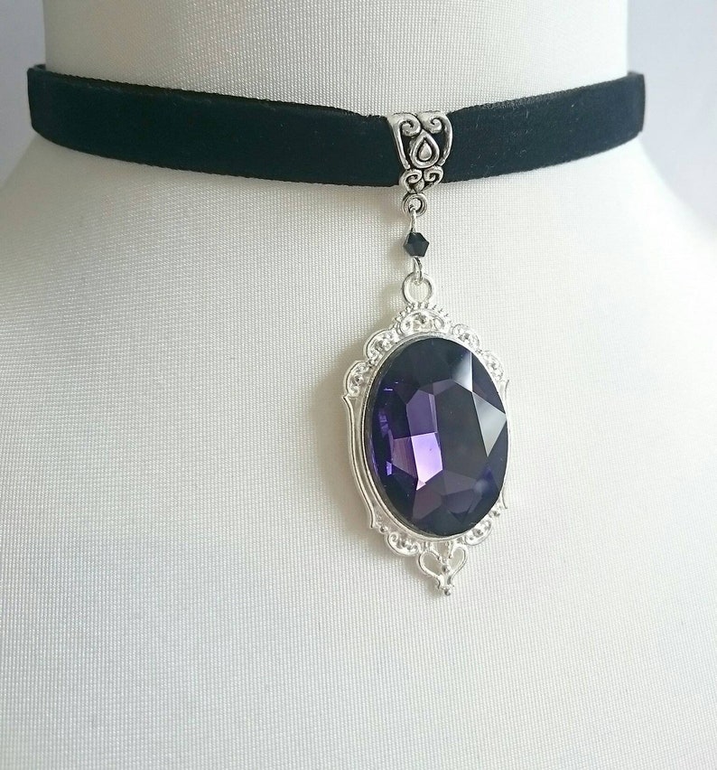 May include: A black velvet choker necklace with a silver pendant featuring a large, faceted purple gemstone.