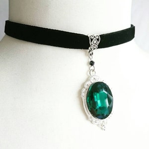 May include: A black velvet choker necklace with a silver pendant featuring a large, emerald green gemstone.