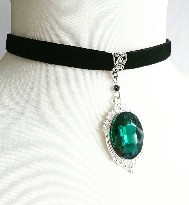 May include: A black velvet choker necklace with a silver pendant featuring a large, emerald green gemstone.