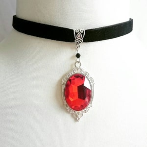 May include: A black velvet choker necklace with a silver pendant featuring a large, red, faceted gemstone.