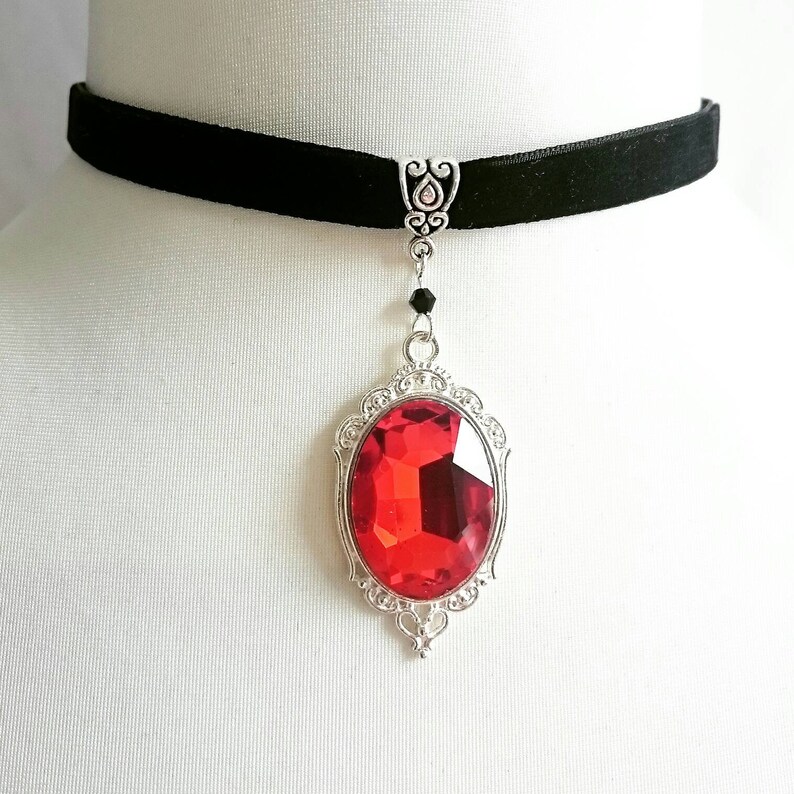 May include: A black velvet choker necklace with a silver pendant featuring a large, red, faceted gemstone.