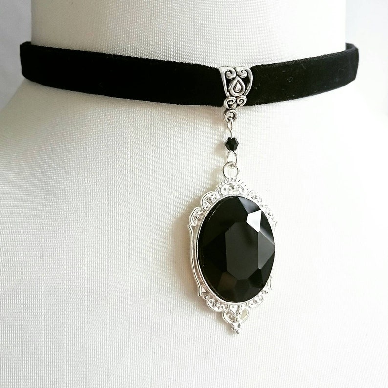 May include: A black velvet choker necklace with a silver pendant featuring a large, faceted black gemstone.