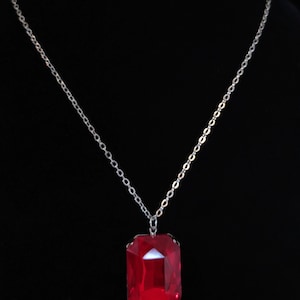 May include: A silver chain necklace with a large, red, faceted gemstone pendant.