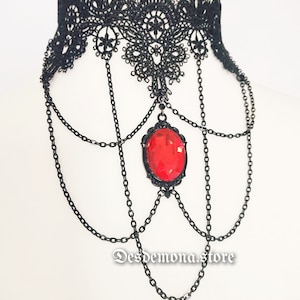 Könnte beinhalten: Schwarze Spitzen-Choker-Halskette mit einem roten Edelstein-Anhänger und mehreren Kettengliedern.