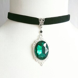 May include: A black velvet choker necklace with a silver pendant featuring a large, emerald green gemstone.