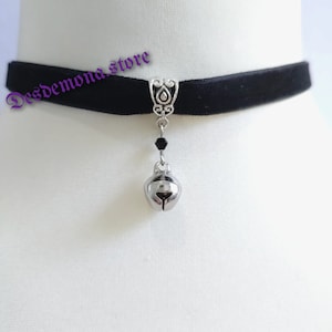 May include: Black velvet choker with a silver bell charm and a black crystal bead.