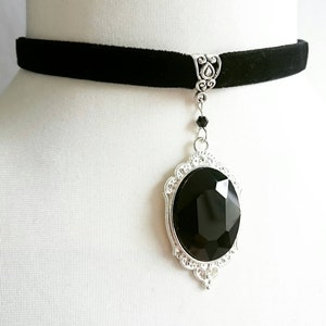 May include: A black velvet choker necklace with a silver pendant featuring a large black faceted gemstone.