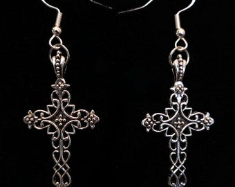 May include: A pair of silver-colored cross earrings. Each earring features an ornate, openwork cross design with intricate details and a decorative hook for pierced ears. The crosses have a vintage or gothic aesthetic.