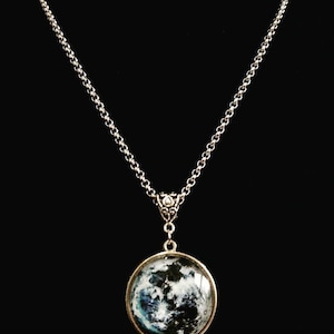 May include: A silver chain necklace with a round pendant featuring a black and white image of the moon.