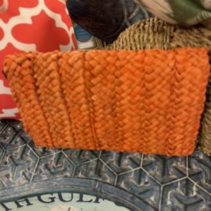 May include: An orange woven basket with a rectangular shape. The basket is made of a textured material and has a slightly curved top edge. The basket is sitting on a blue and white decorative surface.