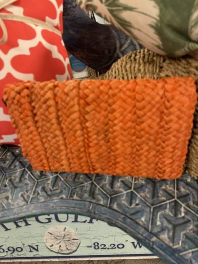 May include: An orange woven basket with a rectangular shape. The basket is made of a textured material and has a slightly curved top edge. The basket is sitting on a blue and white decorative surface.