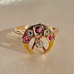 Puede incluir: Un anillo de oro con un diseño de media luna engastado con piedras preciosas rosas y blancas.