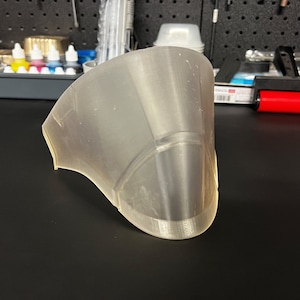 May include: A translucent, white, 3D printed face mask with a geometric design. The mask is made of a smooth, plastic-like material.