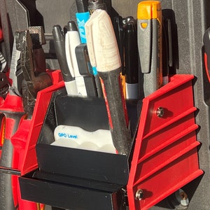 May include: A red and black tool organizer with a black tray and a white label that says "GPO Level". The organizer is filled with various tools, including a yellow and black level, a white marker, and a black pen.