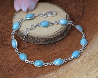 Puede incluir: Un brazalete de cadena de plata con cuentas de piedras azules de forma ovalada. El brazalete tiene un cierre de langosta.