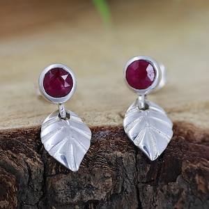 May include: A pair of silver earrings with a red gemstone and a leaf design.