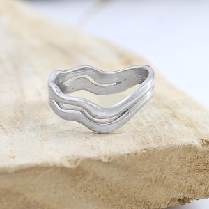 Puede incluir: Un anillo de plata con un diseño ondulado abstracto. El anillo está hecho de dos bandas entrelazadas.