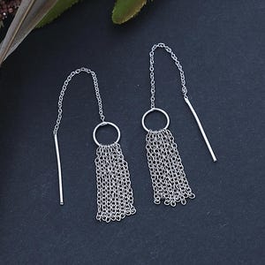 May include: A pair of silver chain earrings with a circle charm and a tassel of multiple chains.