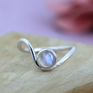 Könnte beinhalten: Ein silberner Ring mit einem zarten Wellenmuster und einem runden Mondstein.