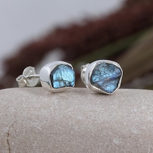 May include: A pair of silver stud earrings with blue labradorite gemstones. The gemstones are irregularly shaped and have a shimmery, iridescent finish.