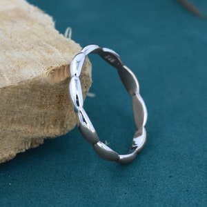 Op de afbeelding: Een zilveren ring met een uniek, golvend ontwerp. De ring is gemaakt van glad, gepolijst metaal en heeft een eenvoudige, elegante uitstraling.