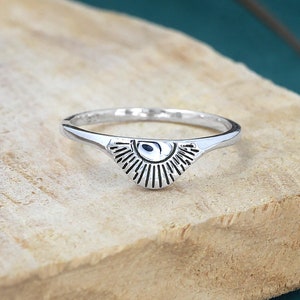 Puede incluir: Anillo de plata con un diseño de sol. El anillo está sobre una superficie de madera.